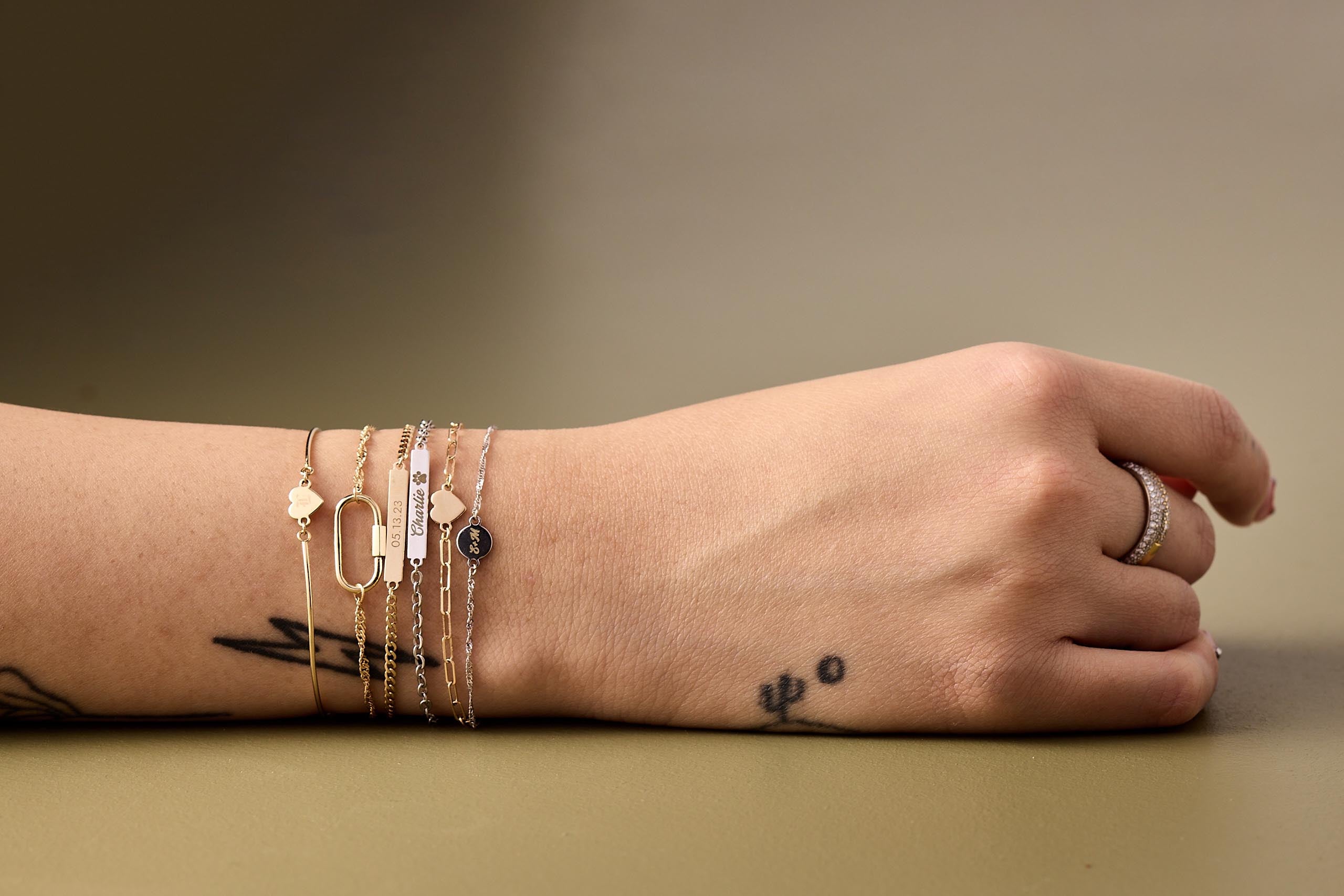 Permanent bracelet stack from Brave Daughters showcasing personalized 14k gold charms, engravings, and welded chains — custom fine jewelry handcrafted in Boston and Providence.