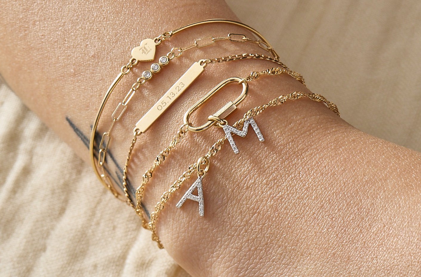 Permanent bracelet stack from Brave Daughters — 14k gold welded chains with custom engraving, diamond initial charms, and symbolic heart detail for a personalized jewelry experience.