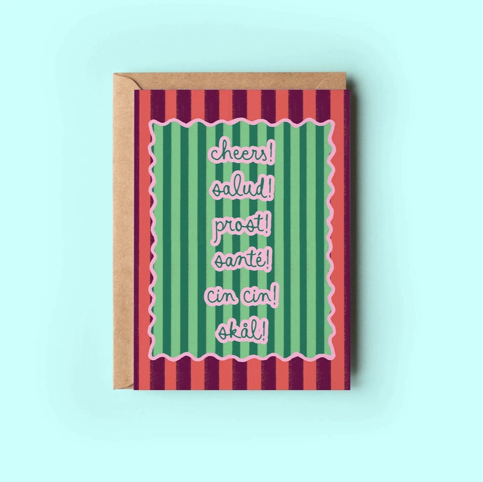 Greeting card featuring colorful stripes and the text "cheers! salud! prost! santé! cin cin! skål!" designed for encouragement and support, accompanied by a brown kraft envelope.