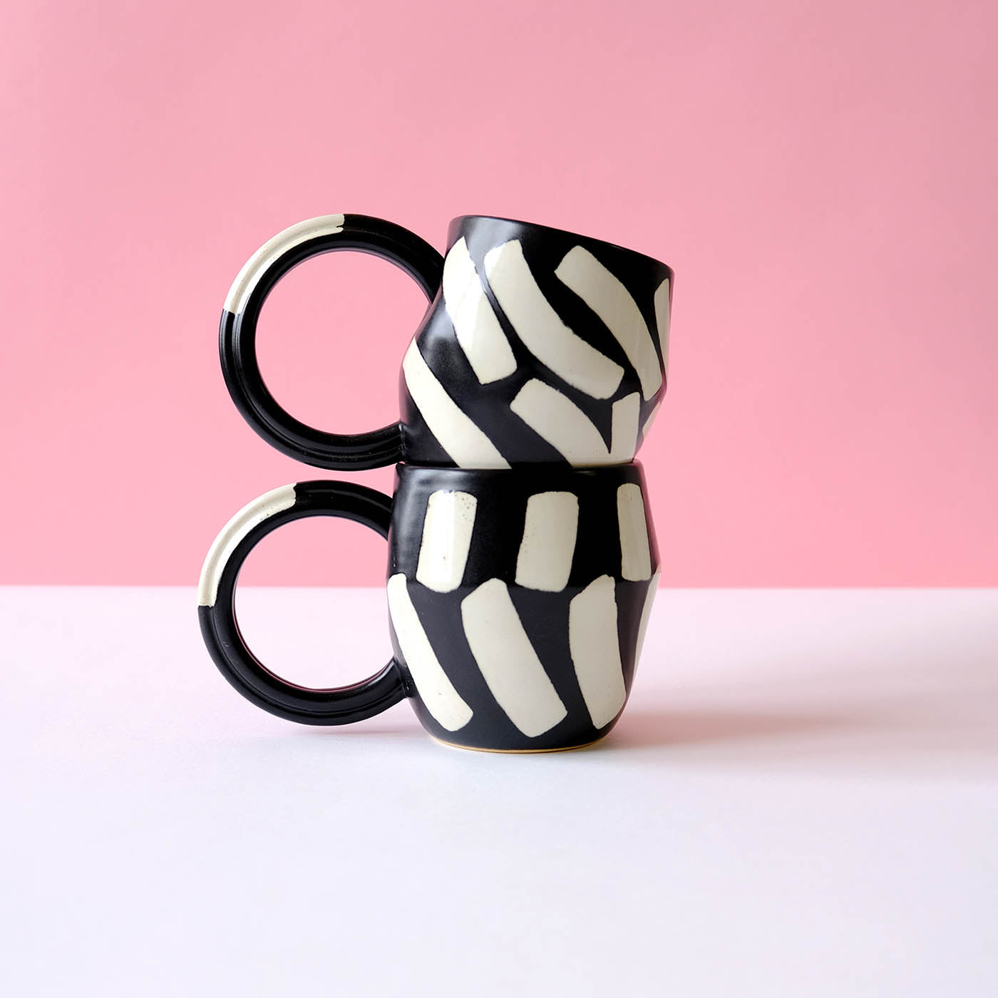 Handcrafted black mug with glossy eggshell shapes, featuring a unique custom-shaped handle, stacked against a pink background, ideal for tea or coffee.