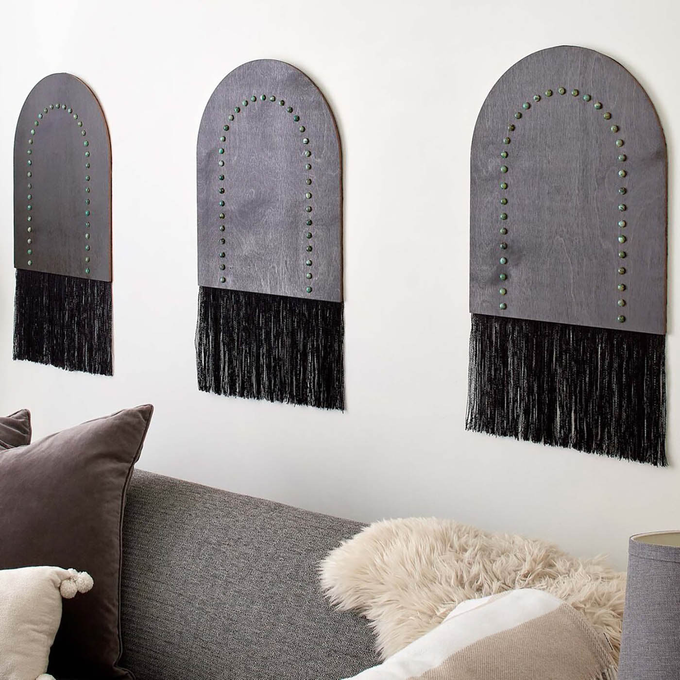Handmade Portal Wall Hanging featuring ebony stained wood, riveted brass, and reclaimed textiles, displayed on a wall above a gray sofa with decorative pillows.