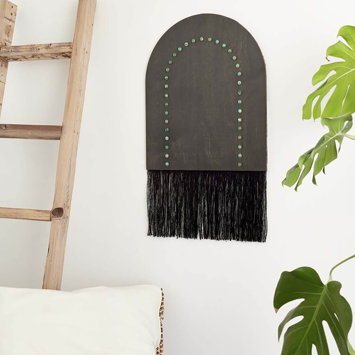 Handmade Portal Wall Hanging featuring ebony stained wood, riveted brass, and reclaimed textiles, displayed on a wall above a gray sofa with decorative pillows.