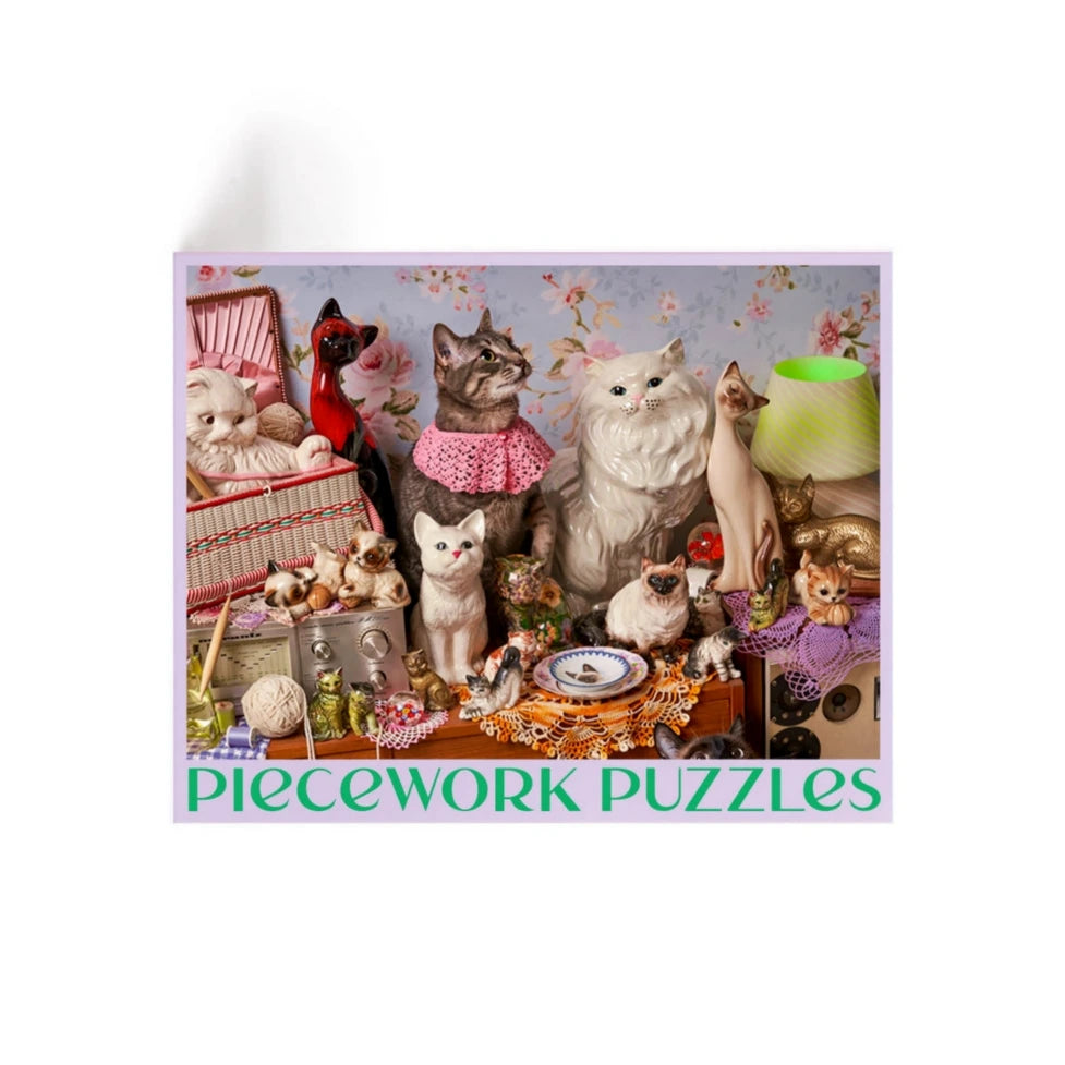 Jigsaw puzzle box with cats and decorative items on a light purple background