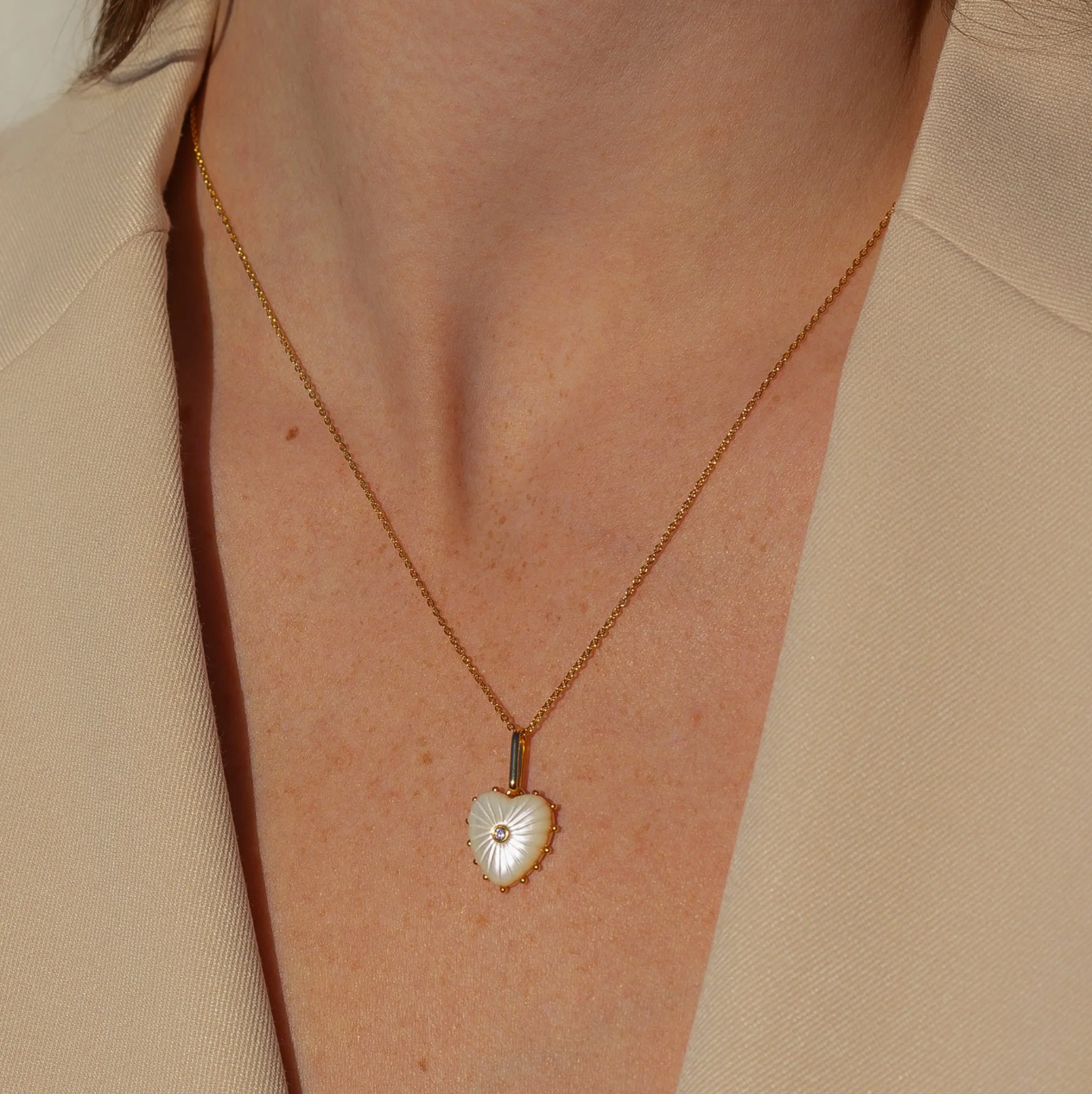 Malene Mother Of Pearl Clip Necklace featuring a hand-carved heart pendant, gold-plated chain, and cubic zirconia accents, displayed elegantly against a neutral background.