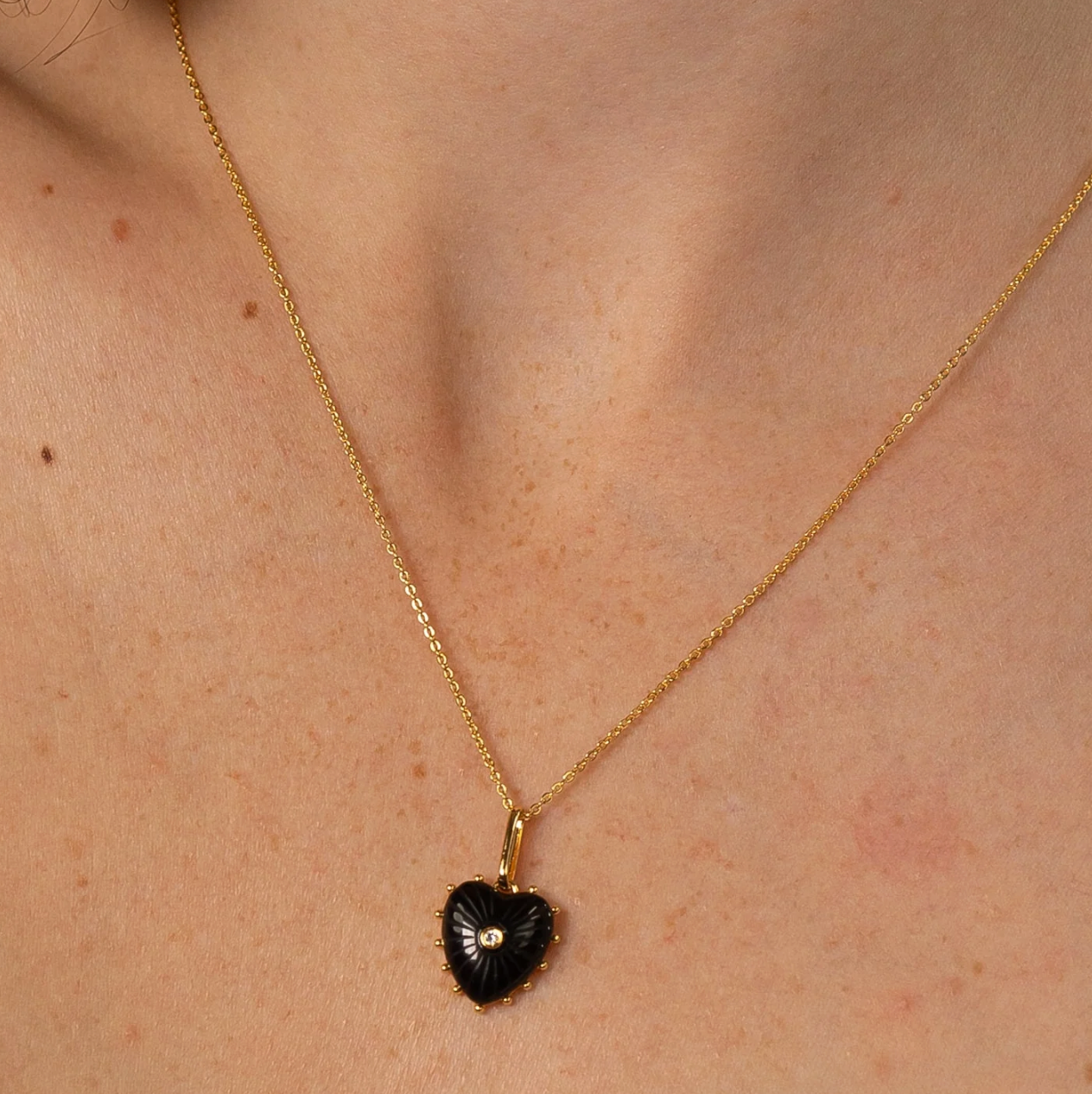 14k gold plated Isabel Heart Charm pendant on a delicate chain, featuring a black heart design with a small gemstone, showcased on a model's neck.