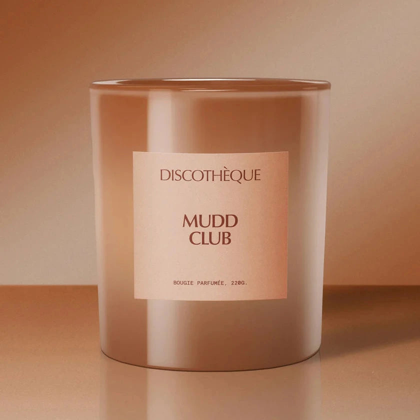 Candle in a metallic container with 'Mudd Club' label on a peach background