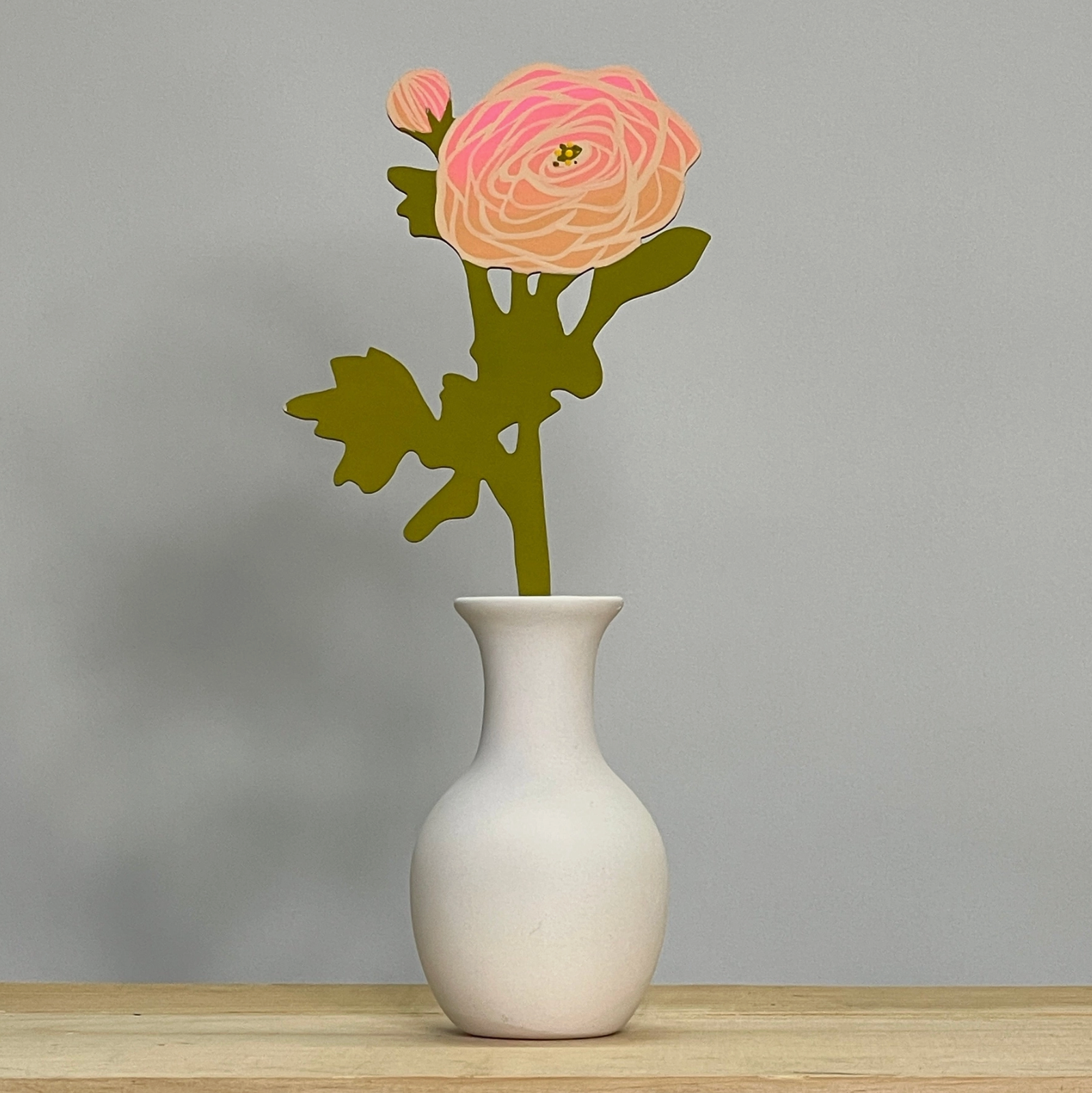 Handcrafted decorative piece featuring a pink ranunculus flower design in a white vase, representing the Forever Flower: Ranunculus by Brave Daughters.