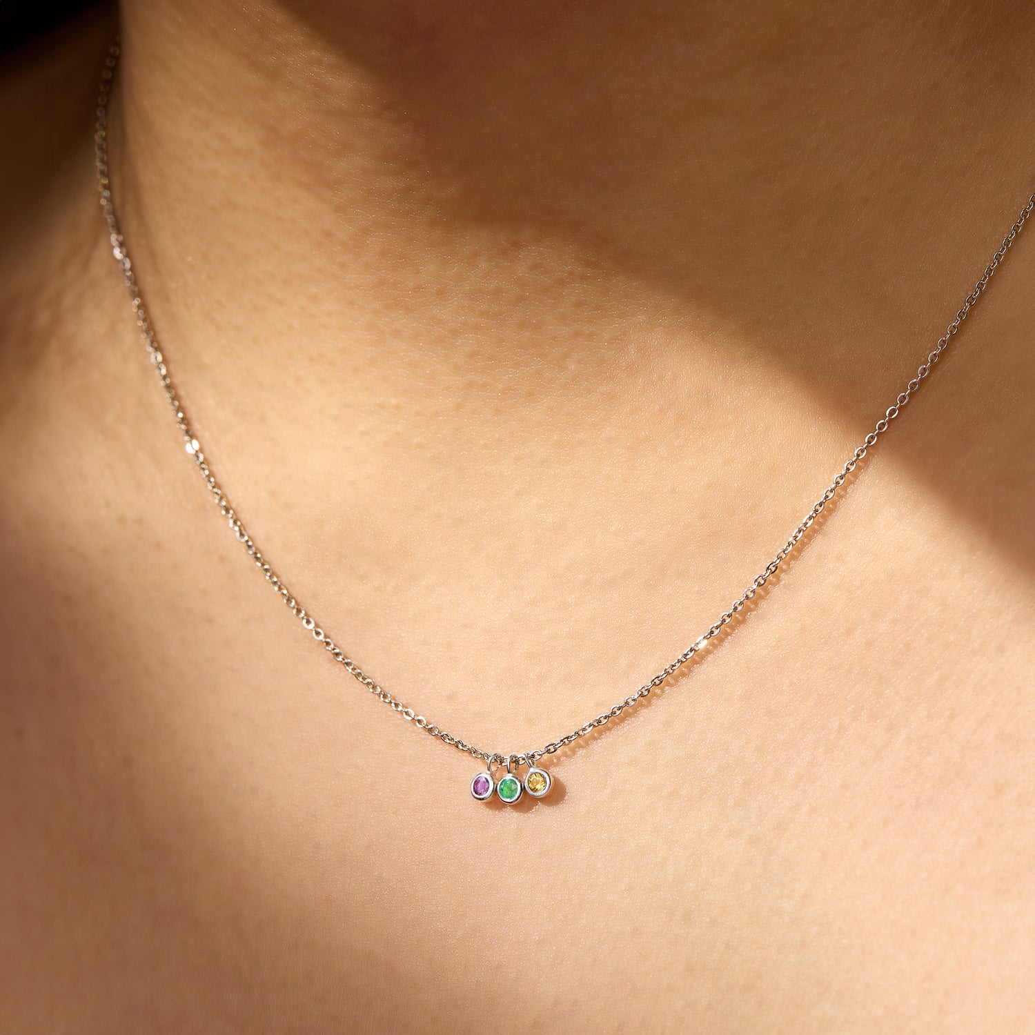 Triple Birthstone Necklace featuring three delicate gemstones on a fine chain, showcased against skin.