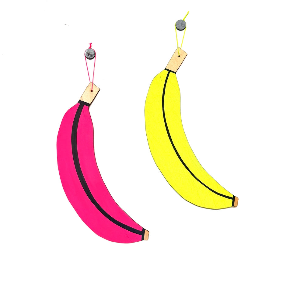 Two banana-shaped objects, one pink and one yellow, hanging against a white background.