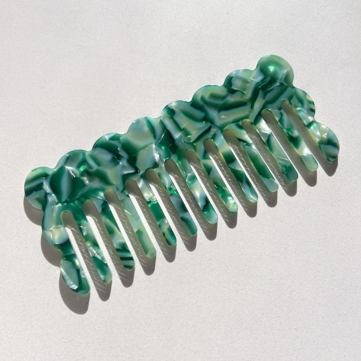 Wavy acetate hair comb in emerald green, featuring a marbled design, suitable for all hair types, emphasizing eco-friendly materials and sustainable practices.