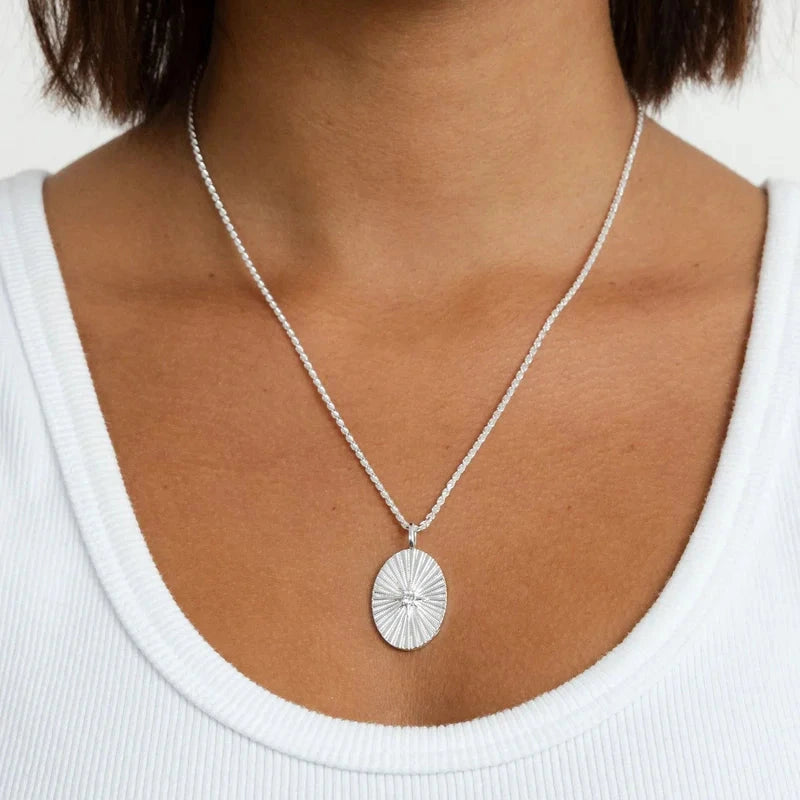 Close-up of a person wearing a silver necklace with a pendant on a white background