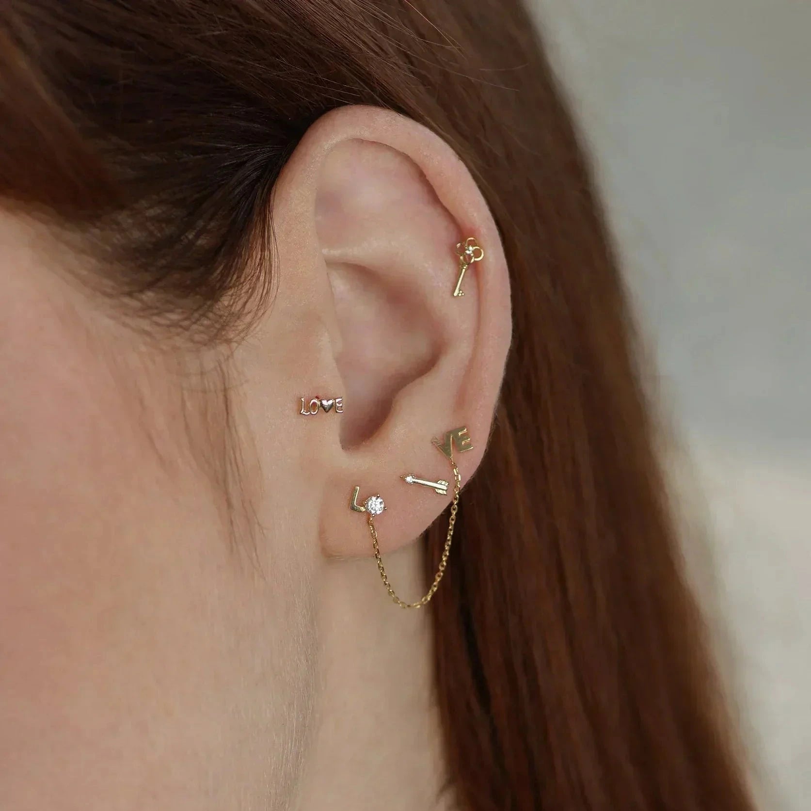 a woman wearing a variety of decorative gold stud earrings including an arrow with a prong set white stone