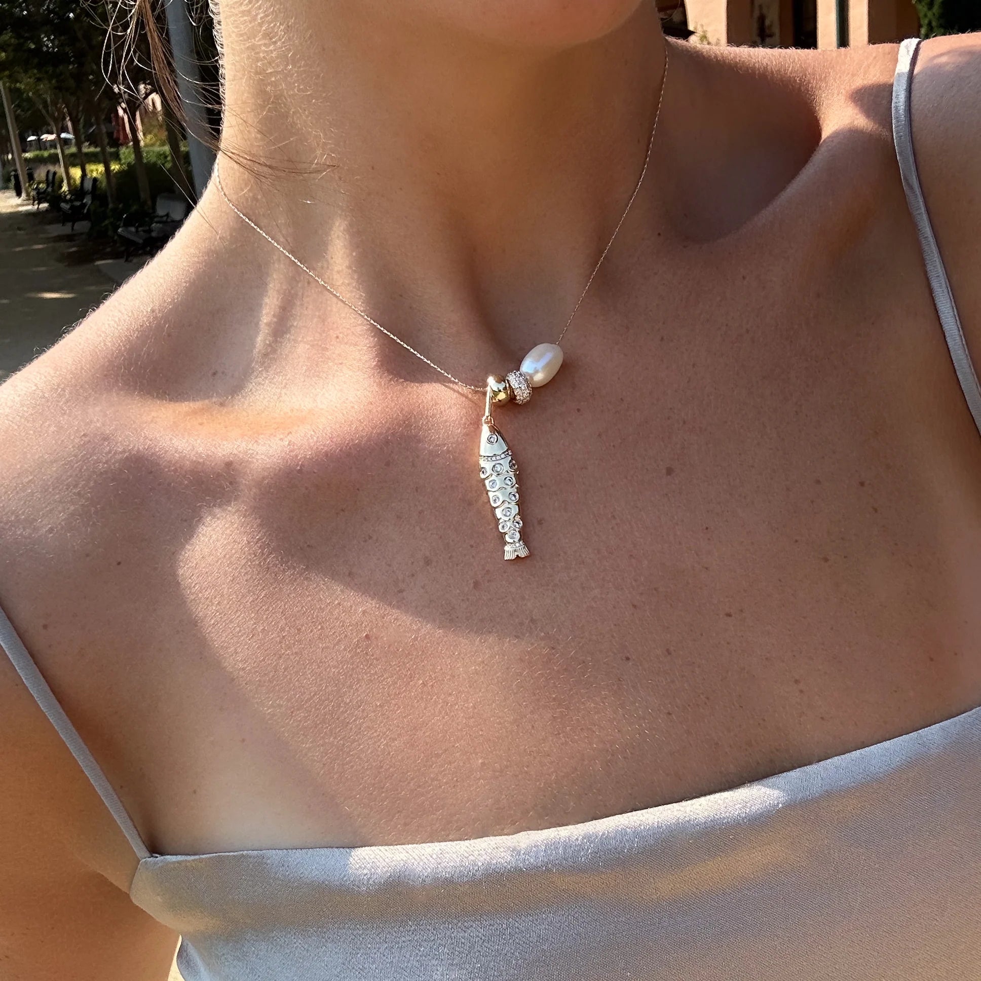 a woman wearing a gold chain necklace with several gold charms including a bead charm over a beige tank top