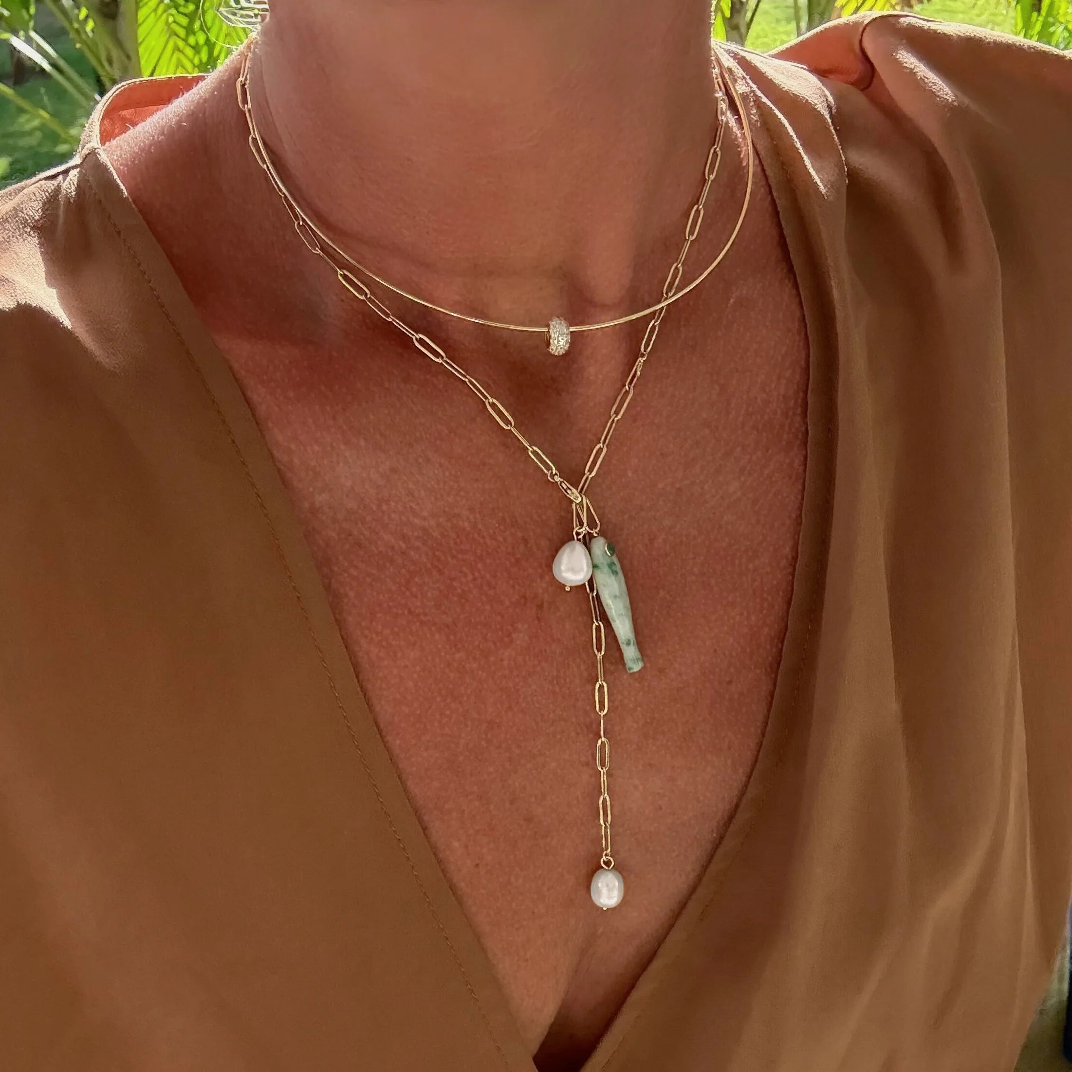 a woman wearing several gold necklaces with various charms including a gold pave bead charm over a brown blouse