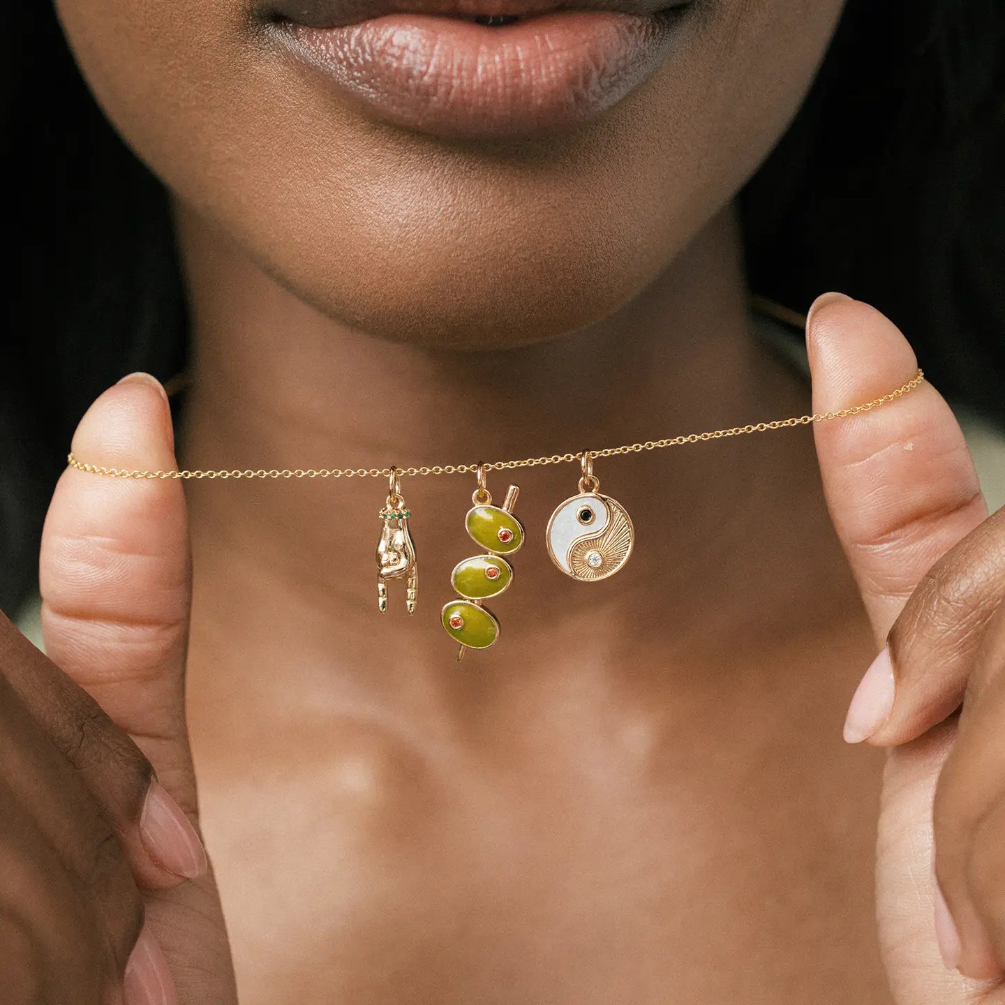 Necklace with three charms held by a person against a neutral background