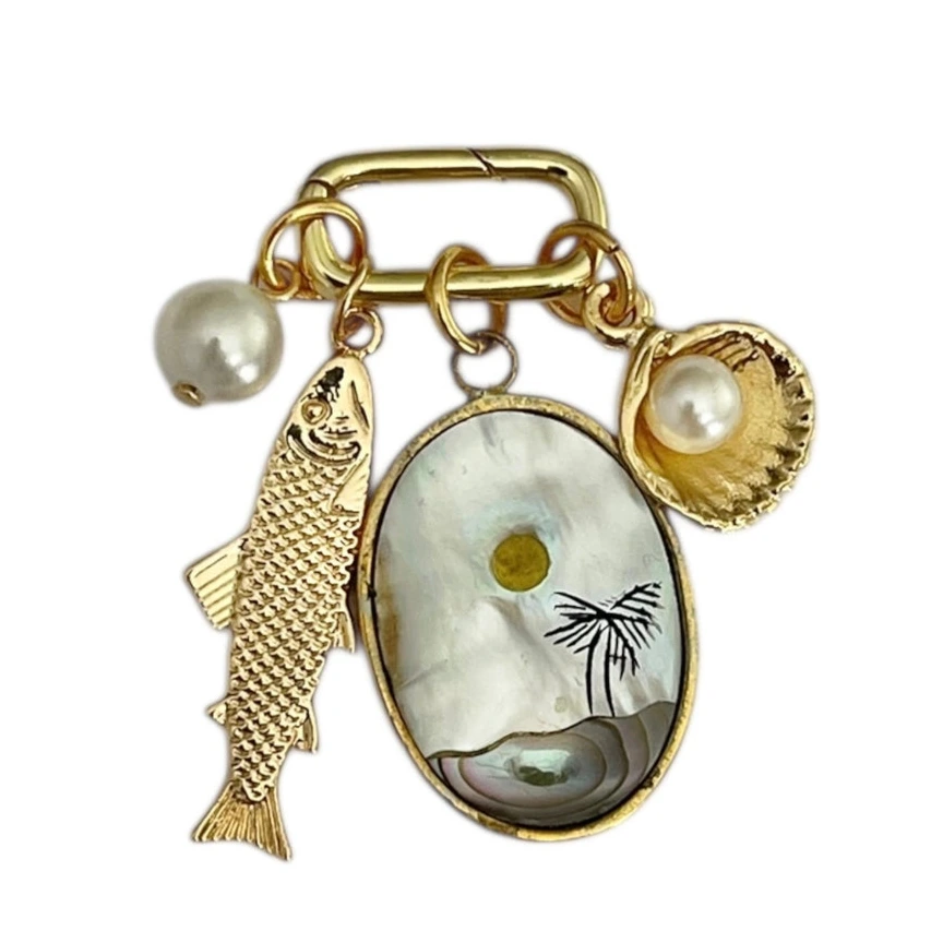 Gold charm with fish, shell, and pearl on a white background