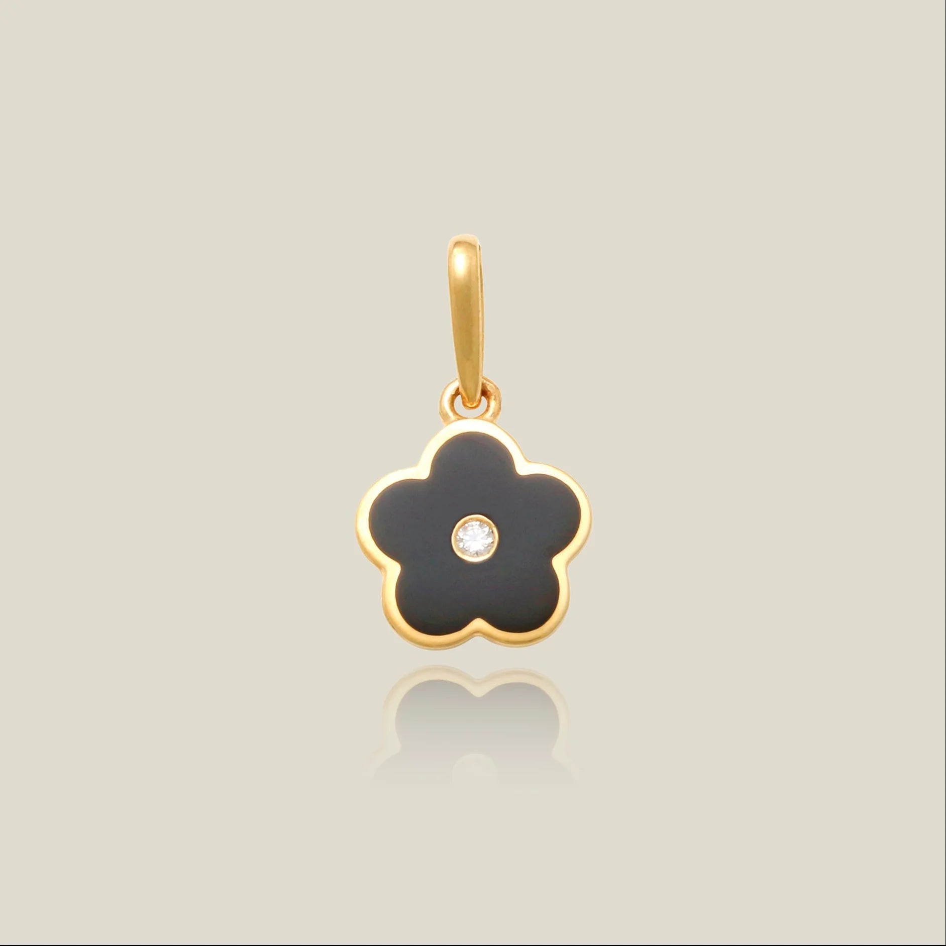 a pendant charm in the shape of a flower with a black enamel flower shape, a gold bezel set, and a bezel set cubic zirconia set in the center over a beige background