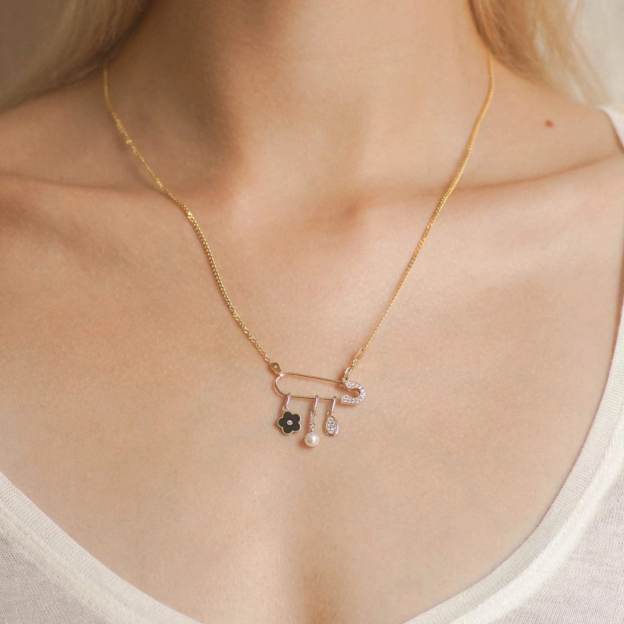 a woman wearing a delicate gold chain with several gold pendant charms hanging from a safety pin shaped charm connector