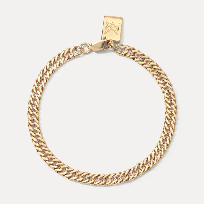 A gold-toned Cuban link chain bracelet with a small square branded tag attached at the clasp, displayed on a light gray background.