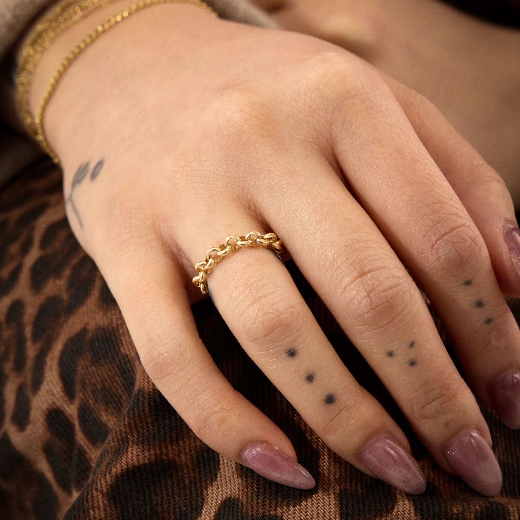 Hand wearing a gold chain ring with leopard print fabric in the background