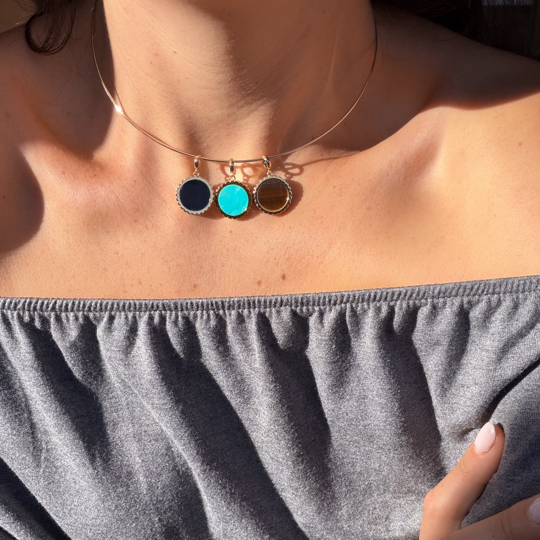 a woman wearing a necklace with three circular gold charms with different color inlay stones over a blue shirt