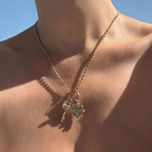 A delicate gold chain necklace with a small ring and dangling floral charms, worn on a model's neck against a blue sky background.