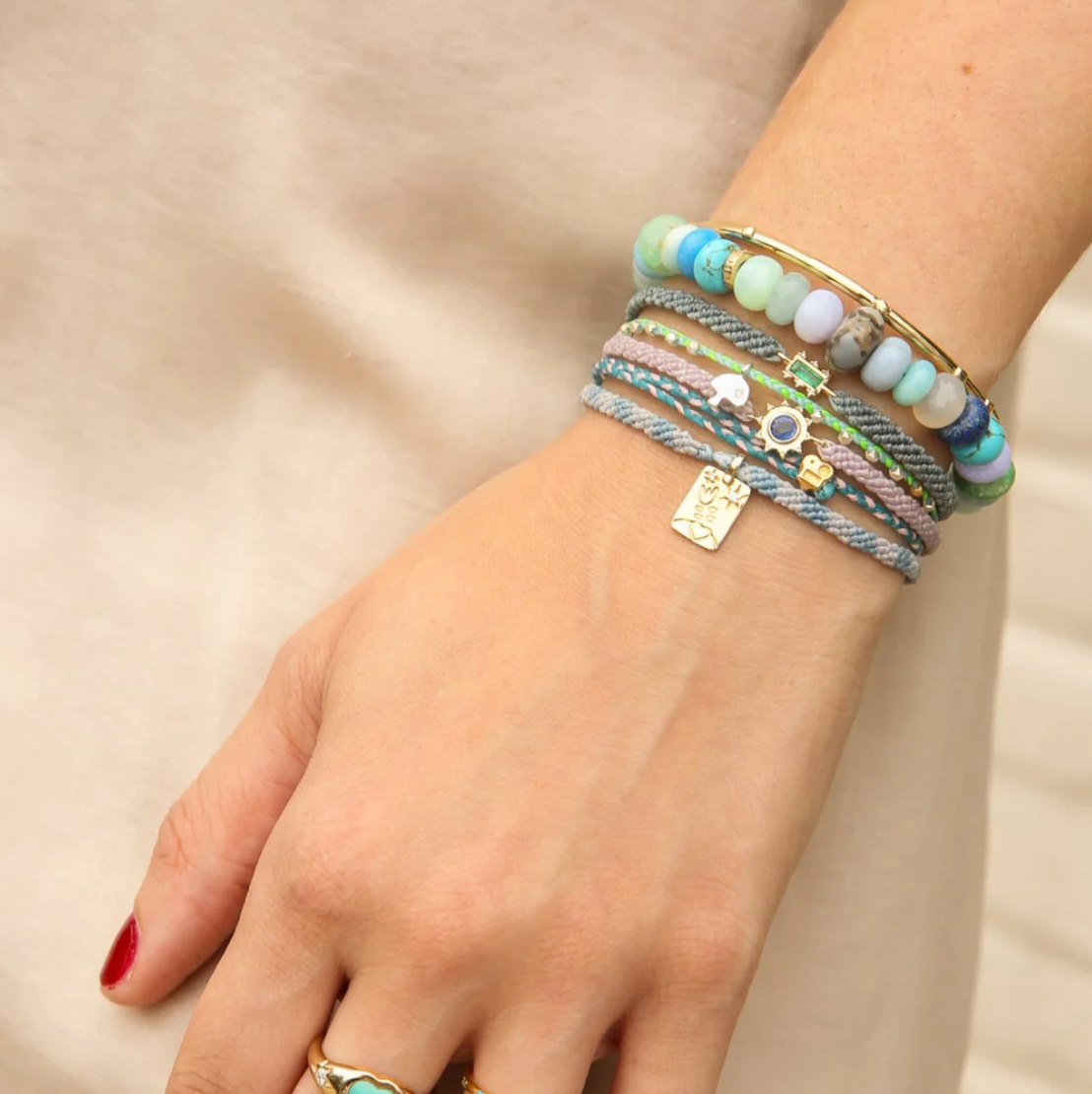 Hand wearing multiple colorful bracelets blue bead on a plain background