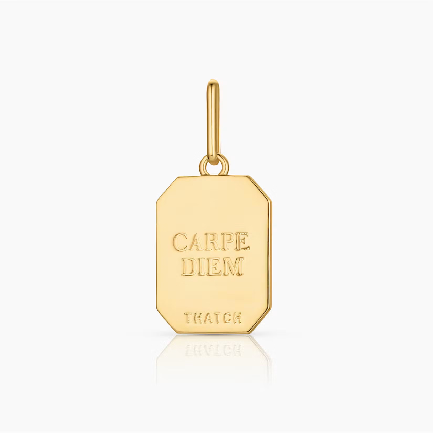 a gold rectangular charm with text engraved reading "carpe diem" and "thatch"
