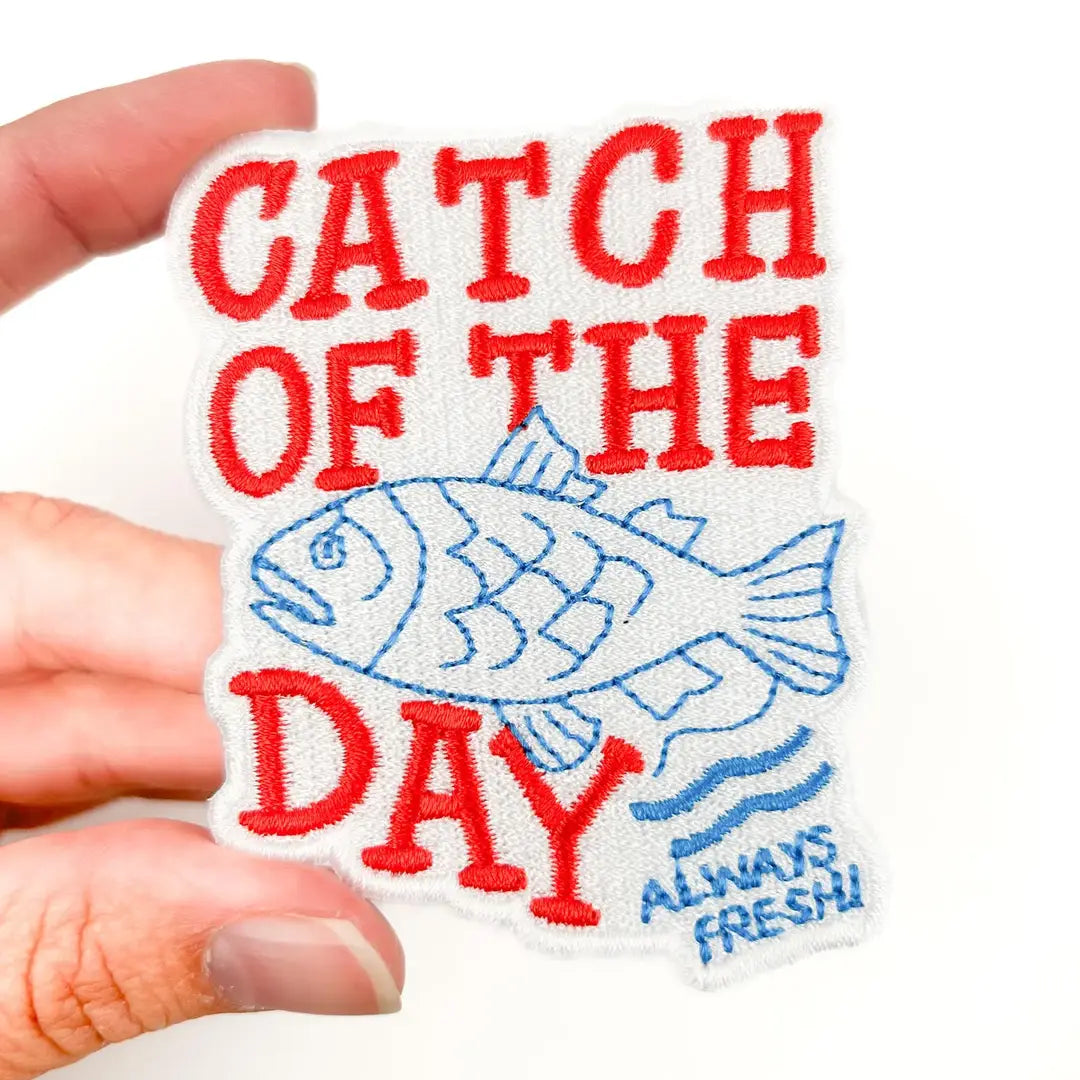 a red and blue patch with text reading catch of the day and a fish illustration with a white background