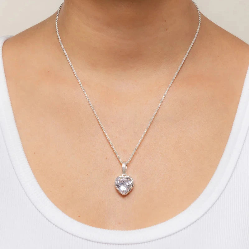 a silver heart shaped pendant worn on the neck of a person wearing a white top