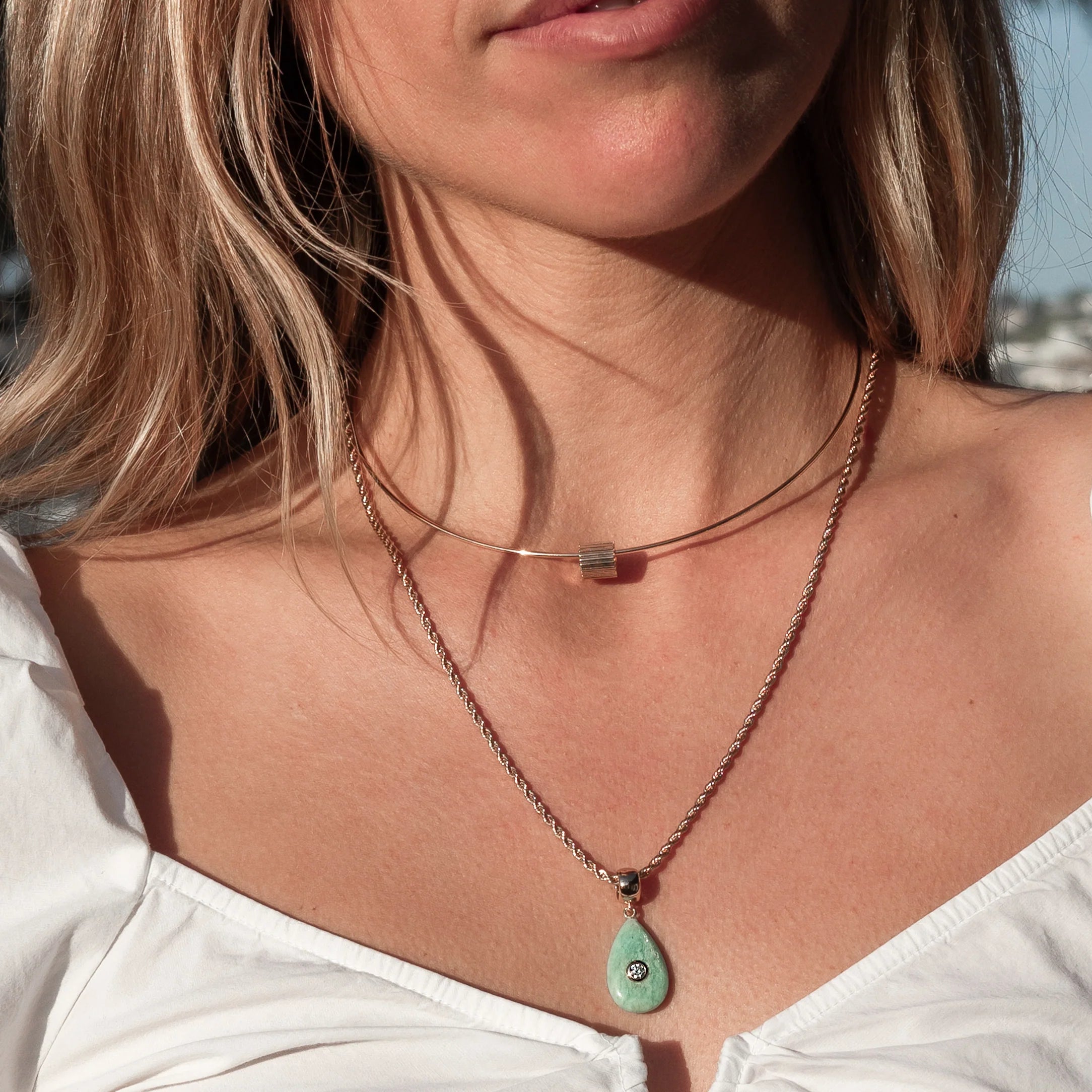a woman wearing a gold necklace with a ridged gold bead charm over a white shirt