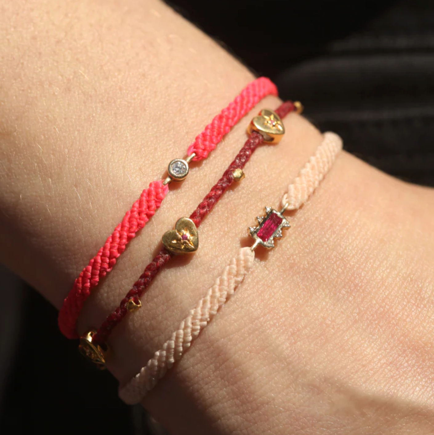 Close-up of a wrist wearing three bracelets with heart and gemstone charms.