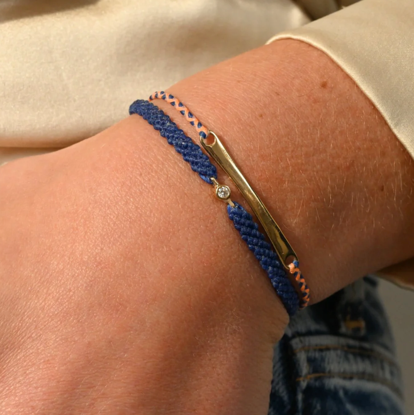 Close-up of a wrist wearing a blue braided nylon bracelet with a 10k gold diamond bezel set diamond