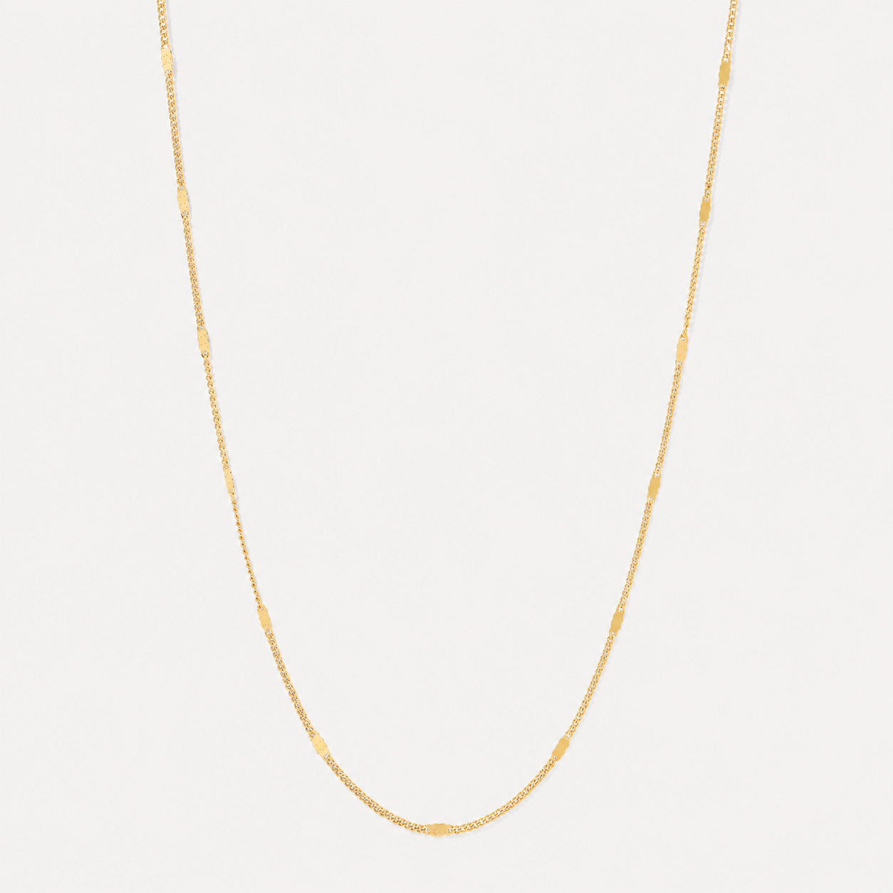 A delicate yellow gold chain necklace with small, spaced-out oval links, displayed against a clean, light off-white background.