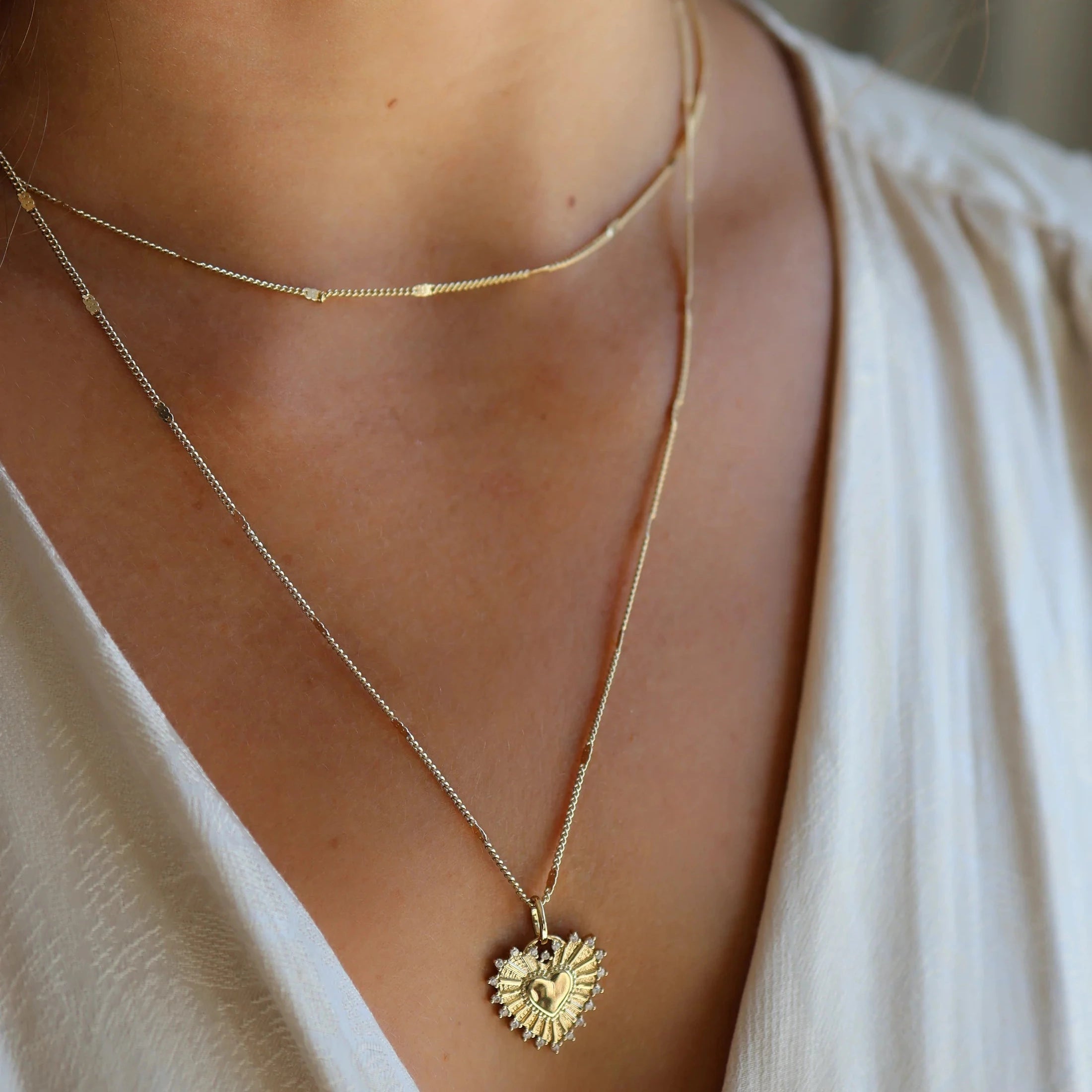 Close-up of a person wearing a gold necklace with a heart pendant.