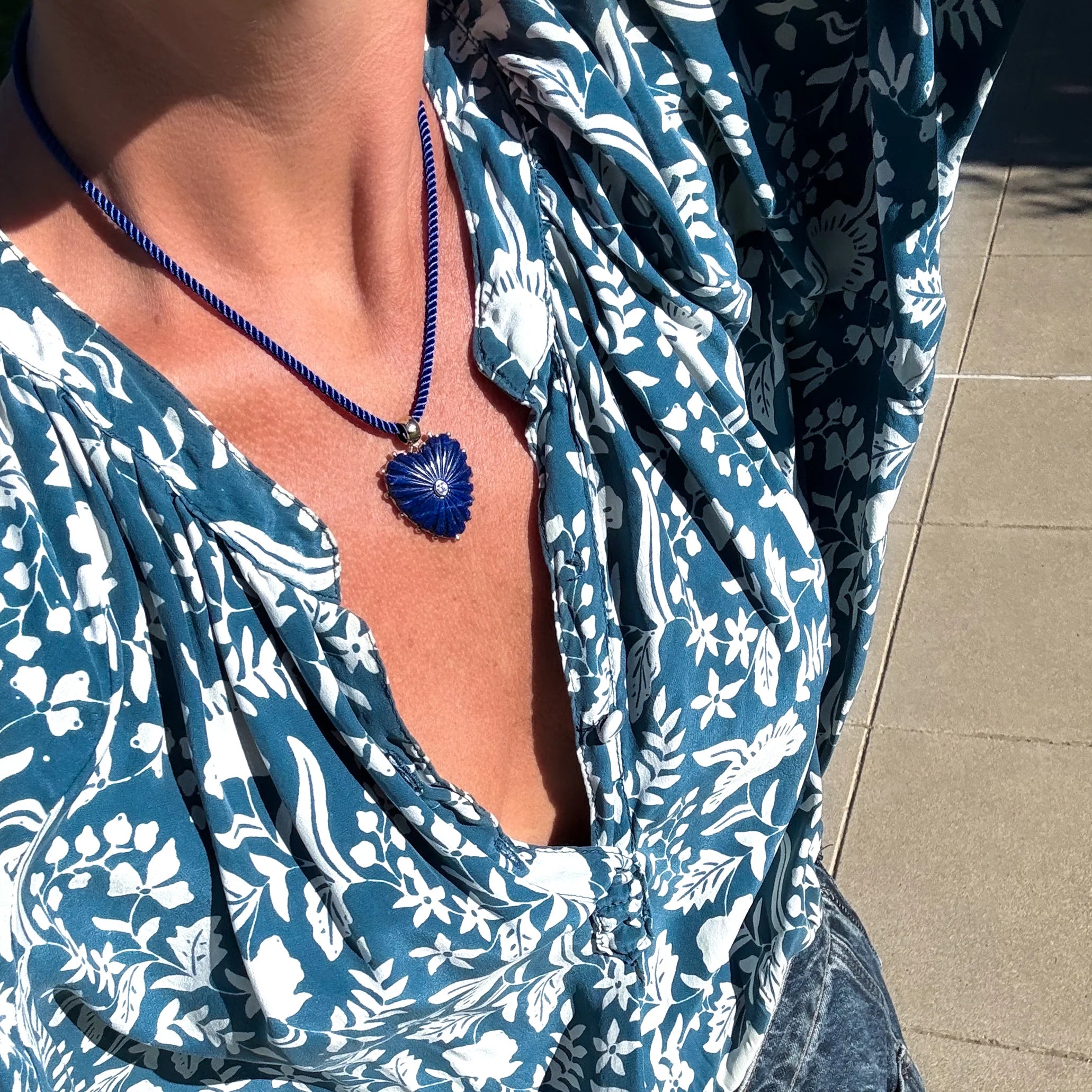 Person wearing a blue and white patterned dress with a necklace featuring a blue pendant.