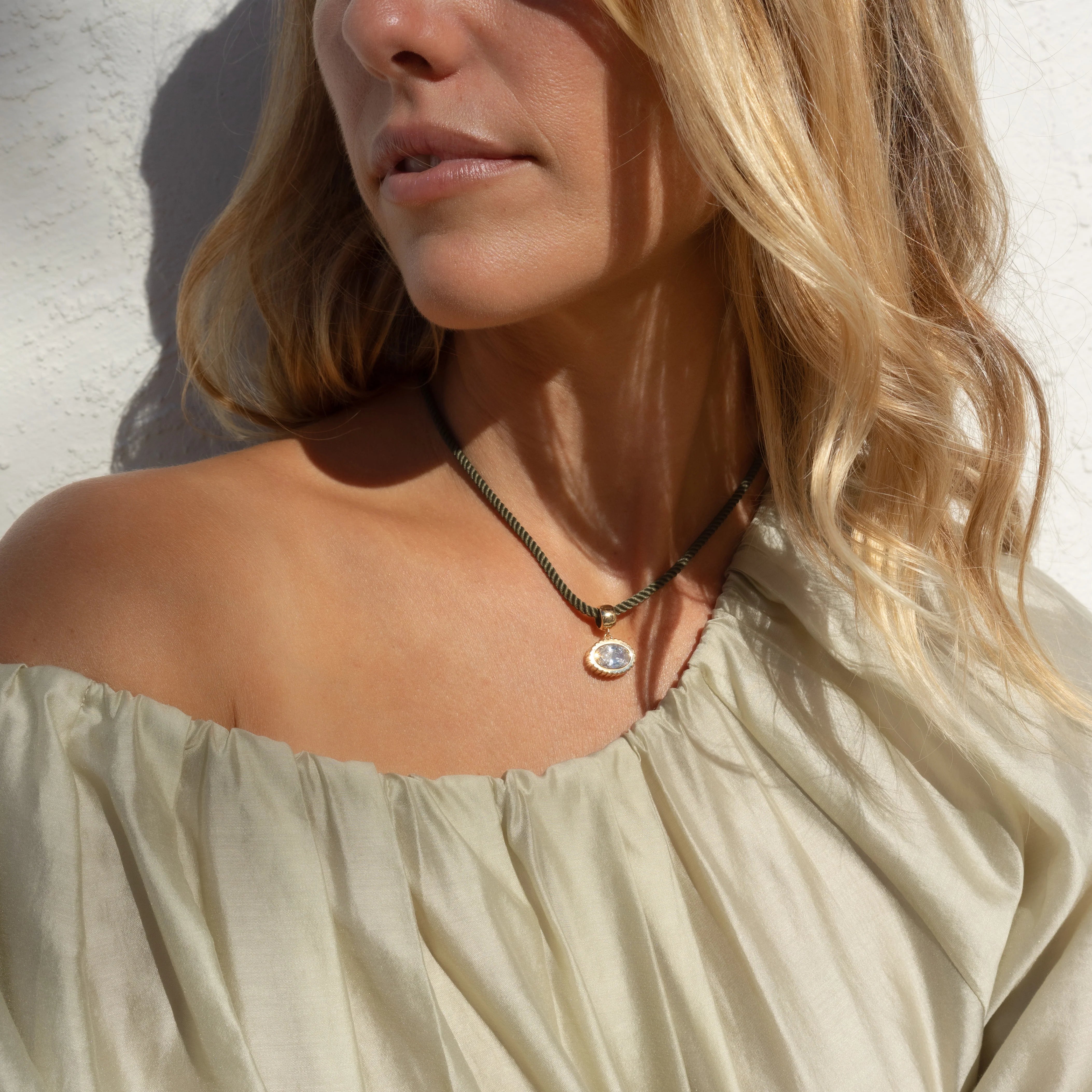 Woman wearing a necklace with a pendant against a light background