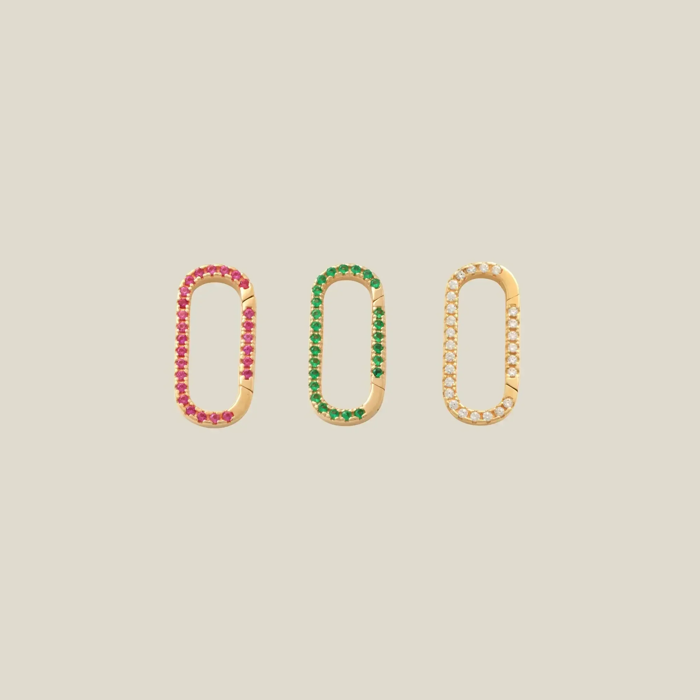 Three gold capsule-shaped charm connectors with rows of colored stones, shown on a plain beige background. The left earring has red stones, the middle has green stones, and the right earring has clear stones.