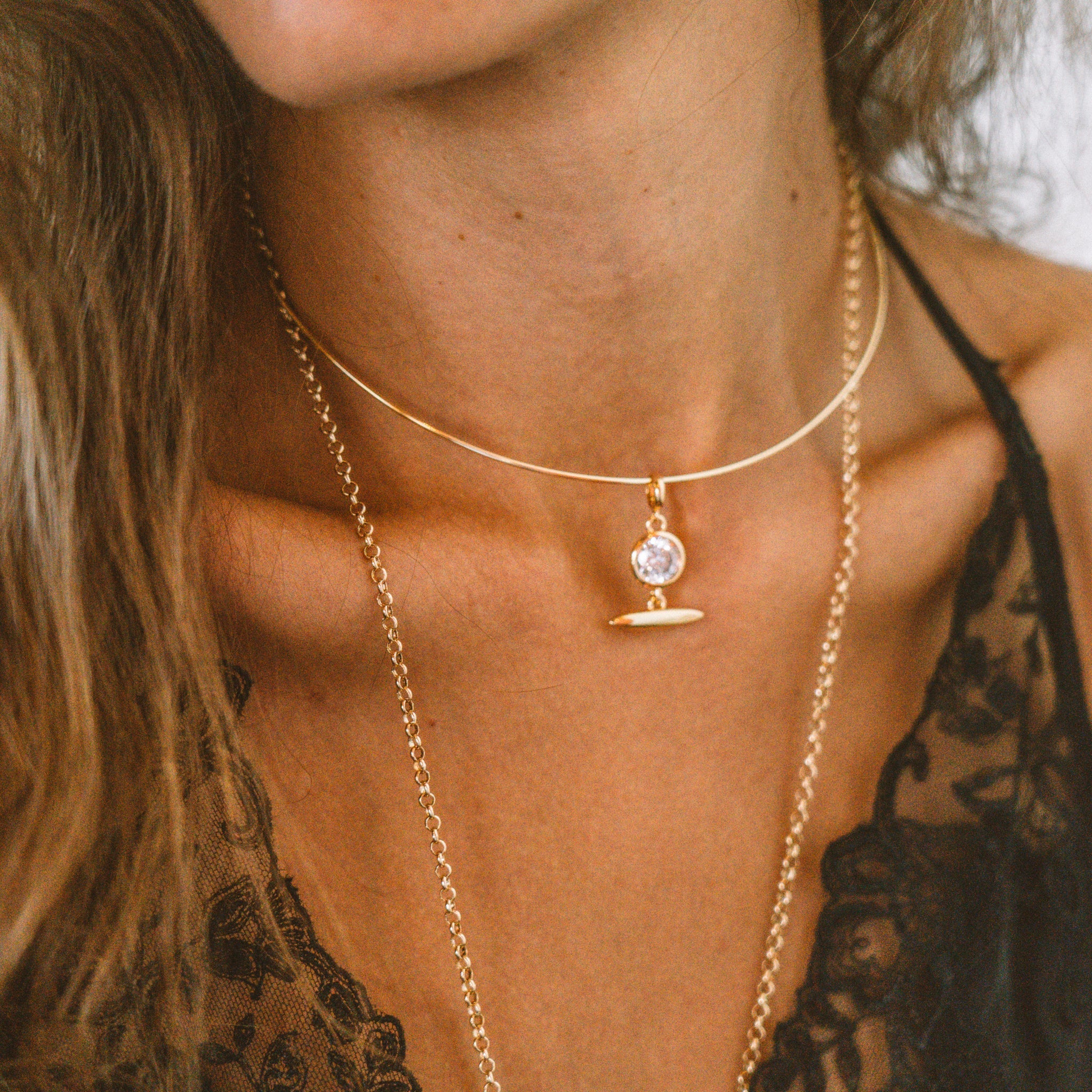 a woman wearing a gold necklace with a gold bezel set cubic zirconia charm with a gold toggle over a black blouse