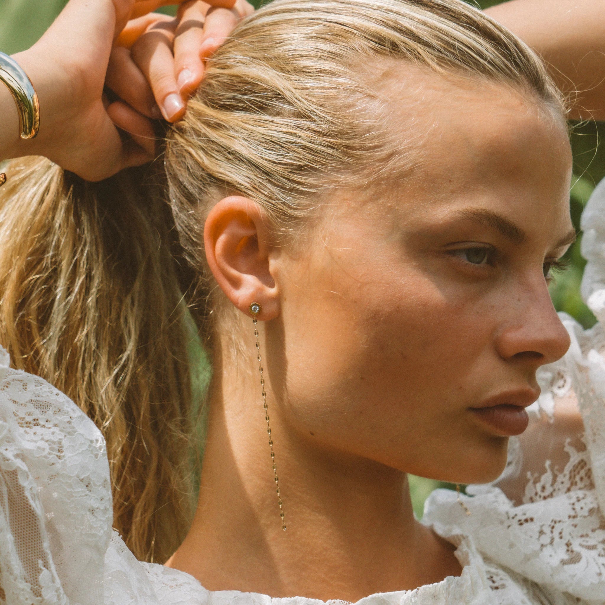 a woman in a white blouse wearing gold stud earrings with white inlay stones and gold chain drops
