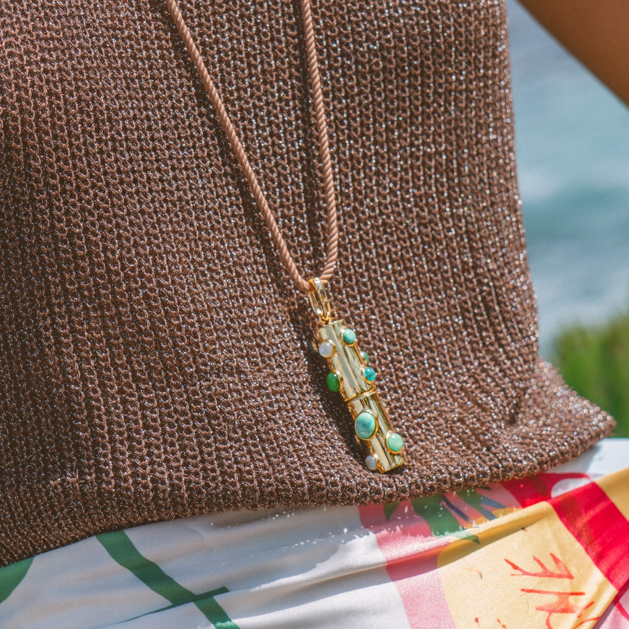 a person wearing a necklace with a gold charm with various blue stones over a brown knit shirt and multicolored dress