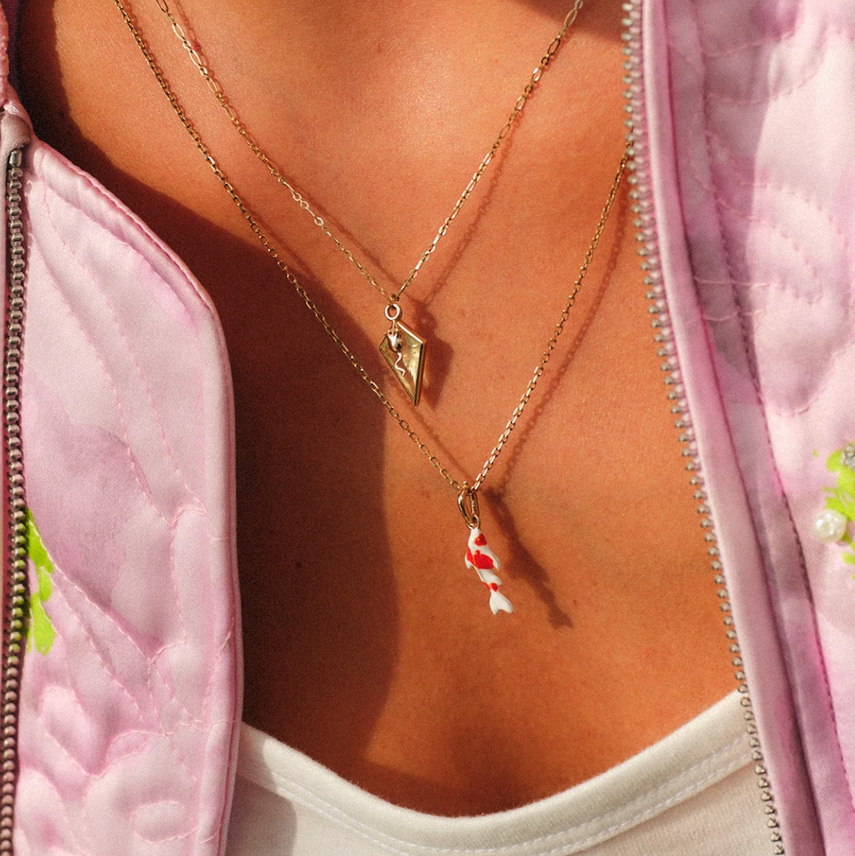 Close-up of a person wearing two gold necklaces with koi enamel pendant 