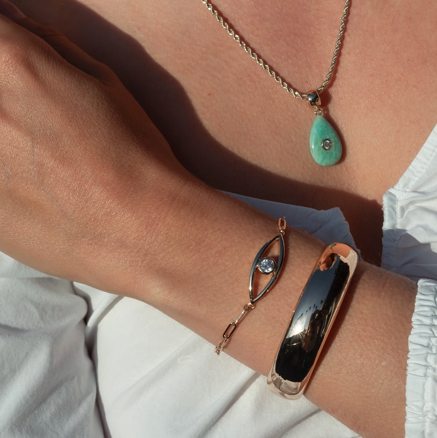 Close-up of a wrist wearing a gold bracelet and a necklace with a green pendant.