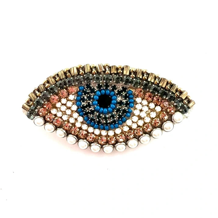 a blue white and gold brooch in the shape of an evil eye on a white background