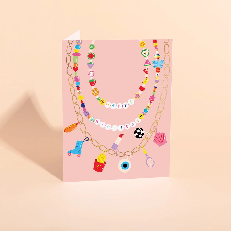 a greeting card with a pink background and an illustration of a beaded charm necklace with assorted colorful beads and letter beads reading happy birthday