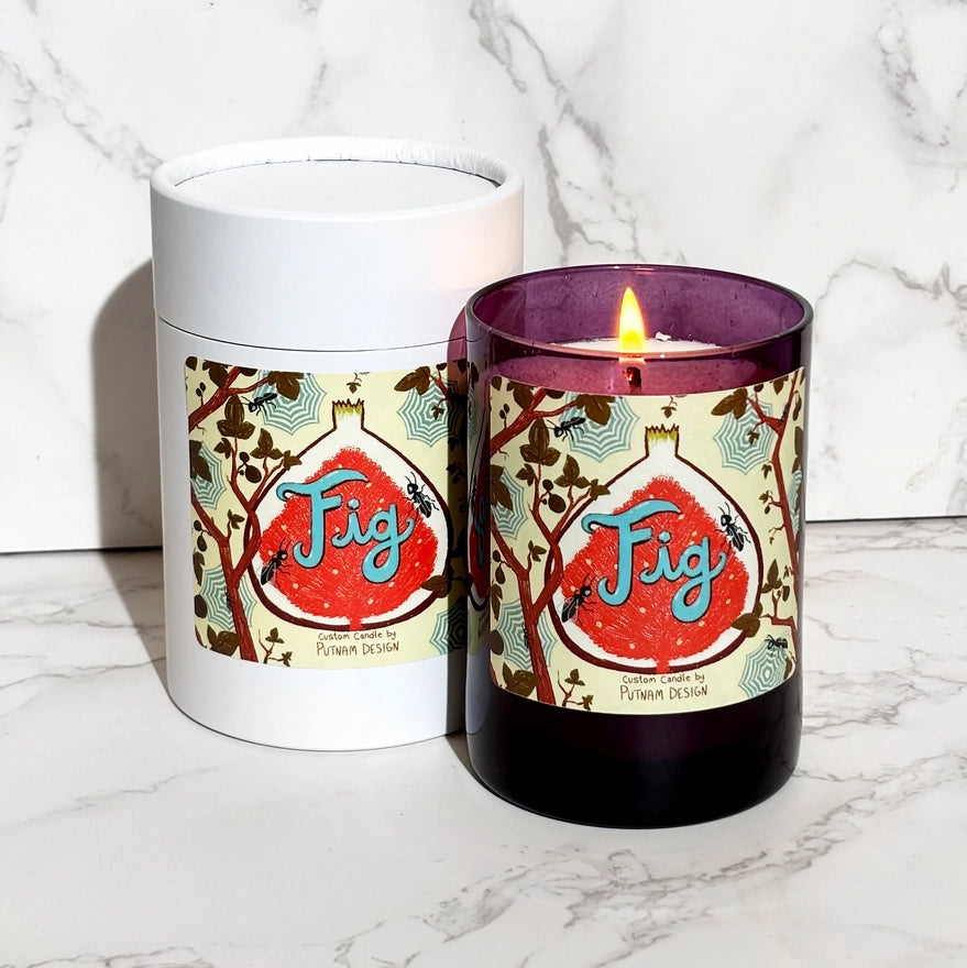 a purple candle with a multicolored label with text reading fig and spider web motif illustrations over a marble background