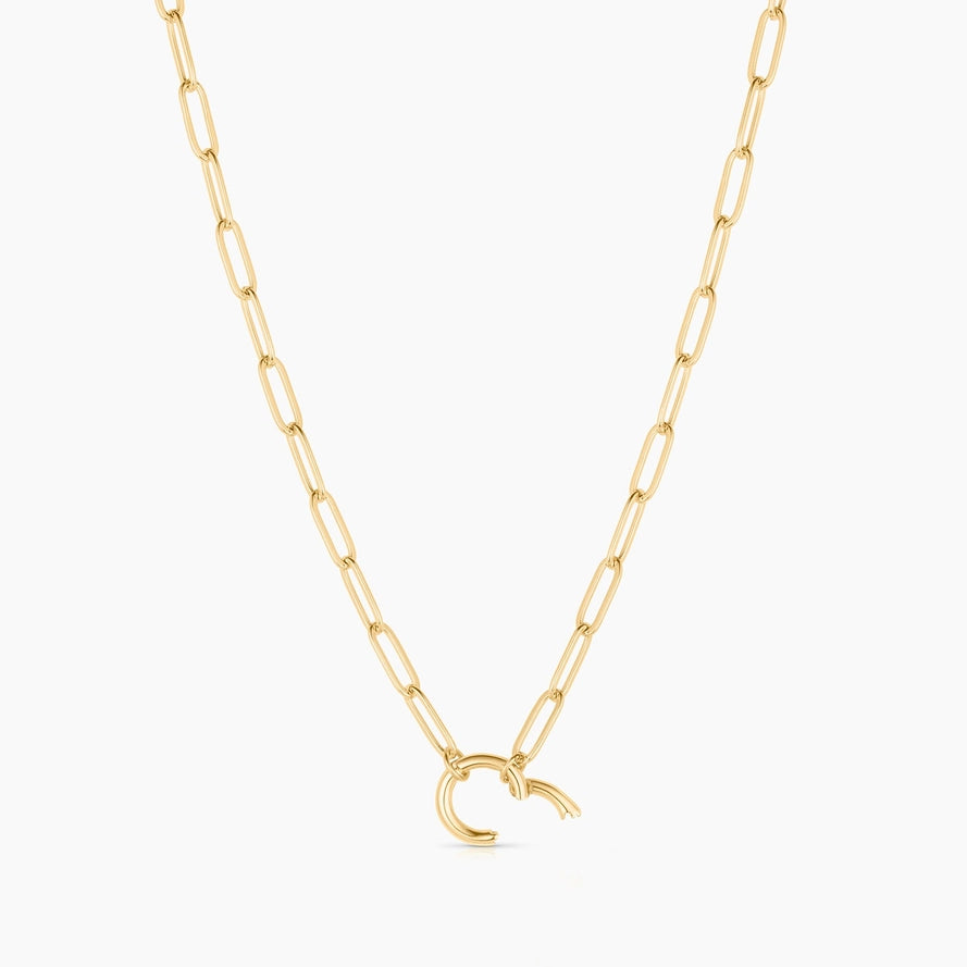 a gold paperclip chain necklace with a gold hinge clip charm on a white background