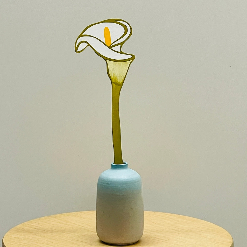 a wooden flower calla lily in a blue vase on a wooden table with a grey background