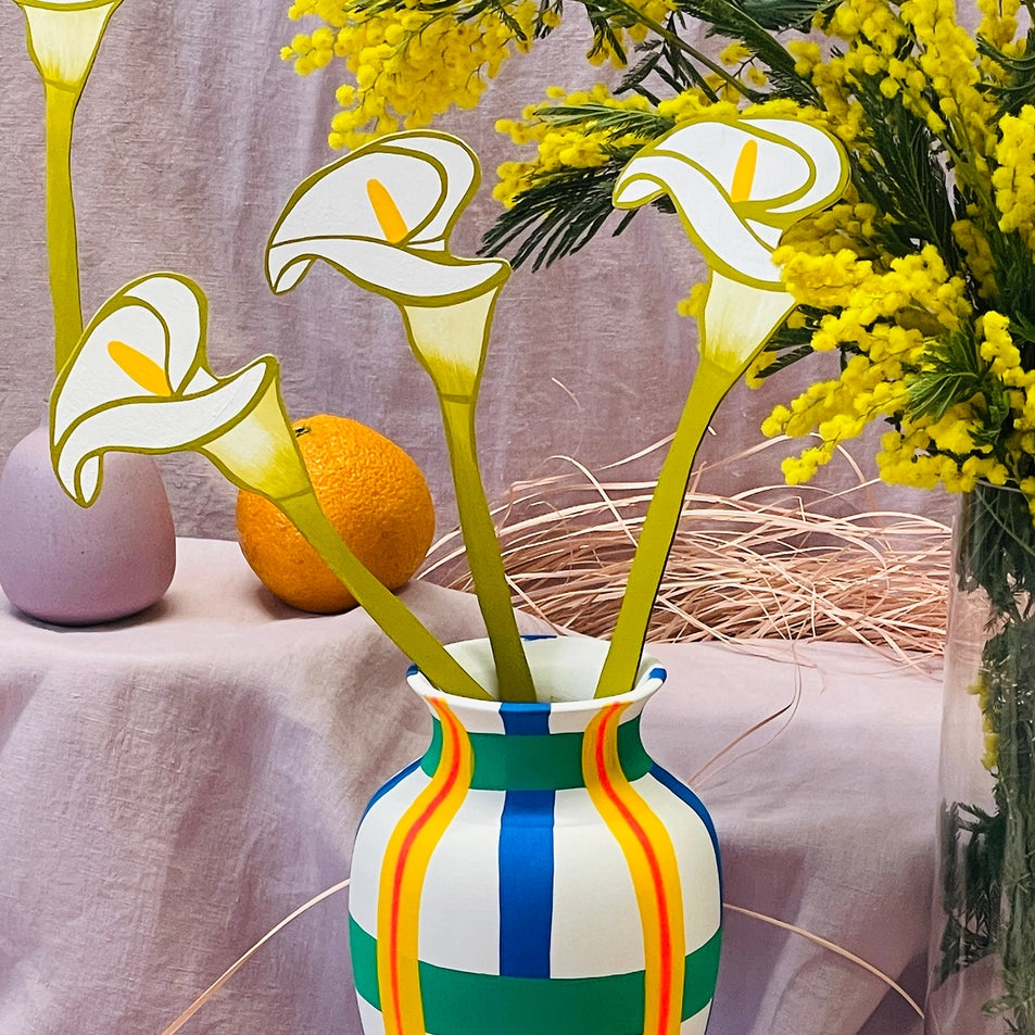 Decorative vase with colorful stripes containing flowers on a tablecloth.