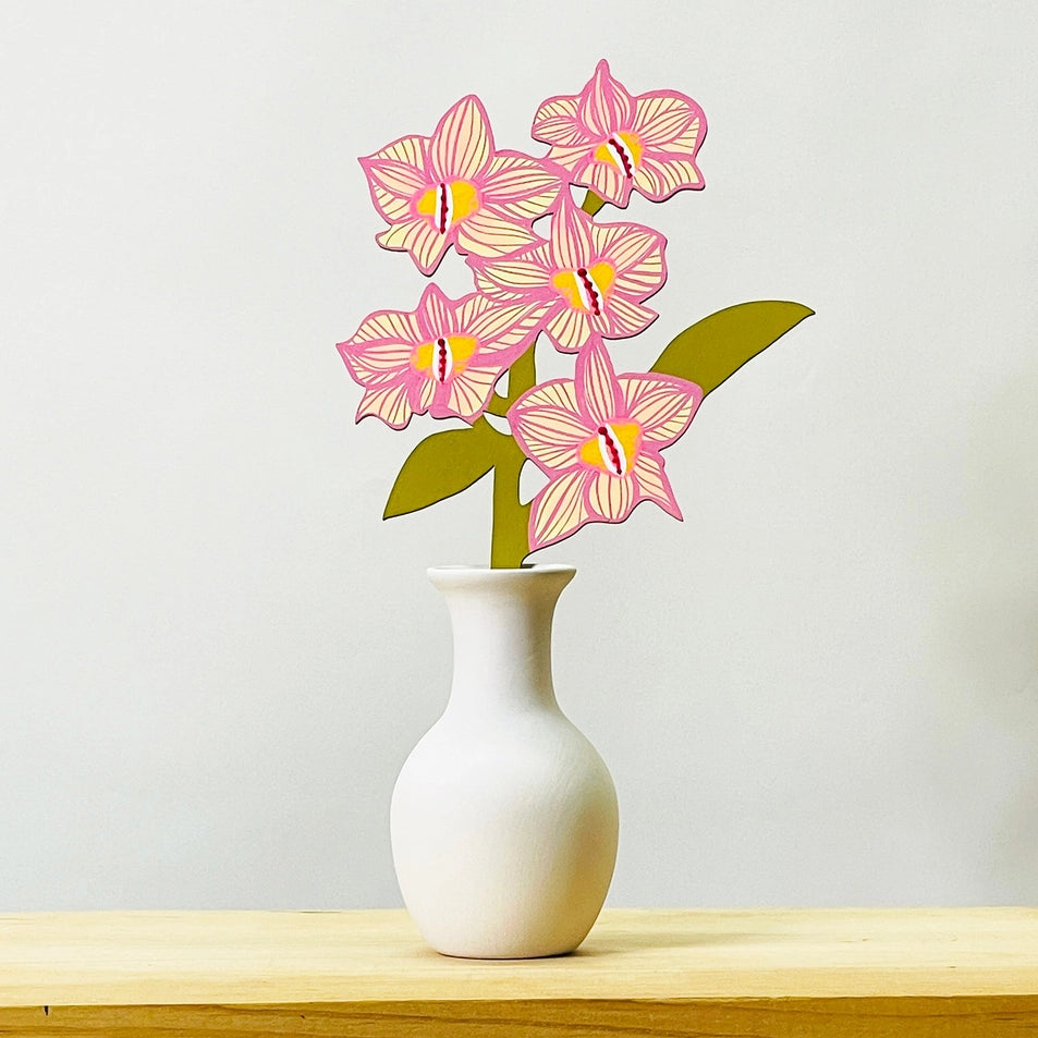 a painted wooden flower in a white vase on a wooden table with a light grey background